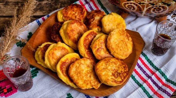 Traditional Romanian and Ukranian cheese pancakes cooked in local rustic style on a traditionally decorated tablecloth and two glasses with local drink