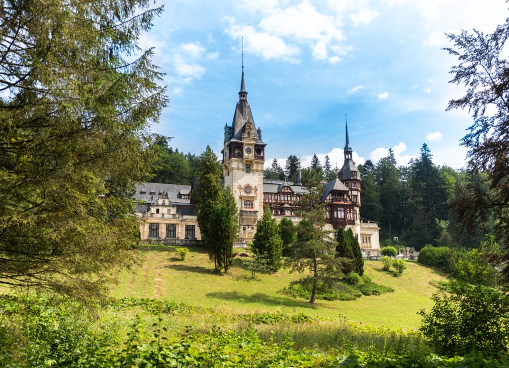View of The Peles Castle in Romania. Castle with gardens in Carpathians, lush forest around it